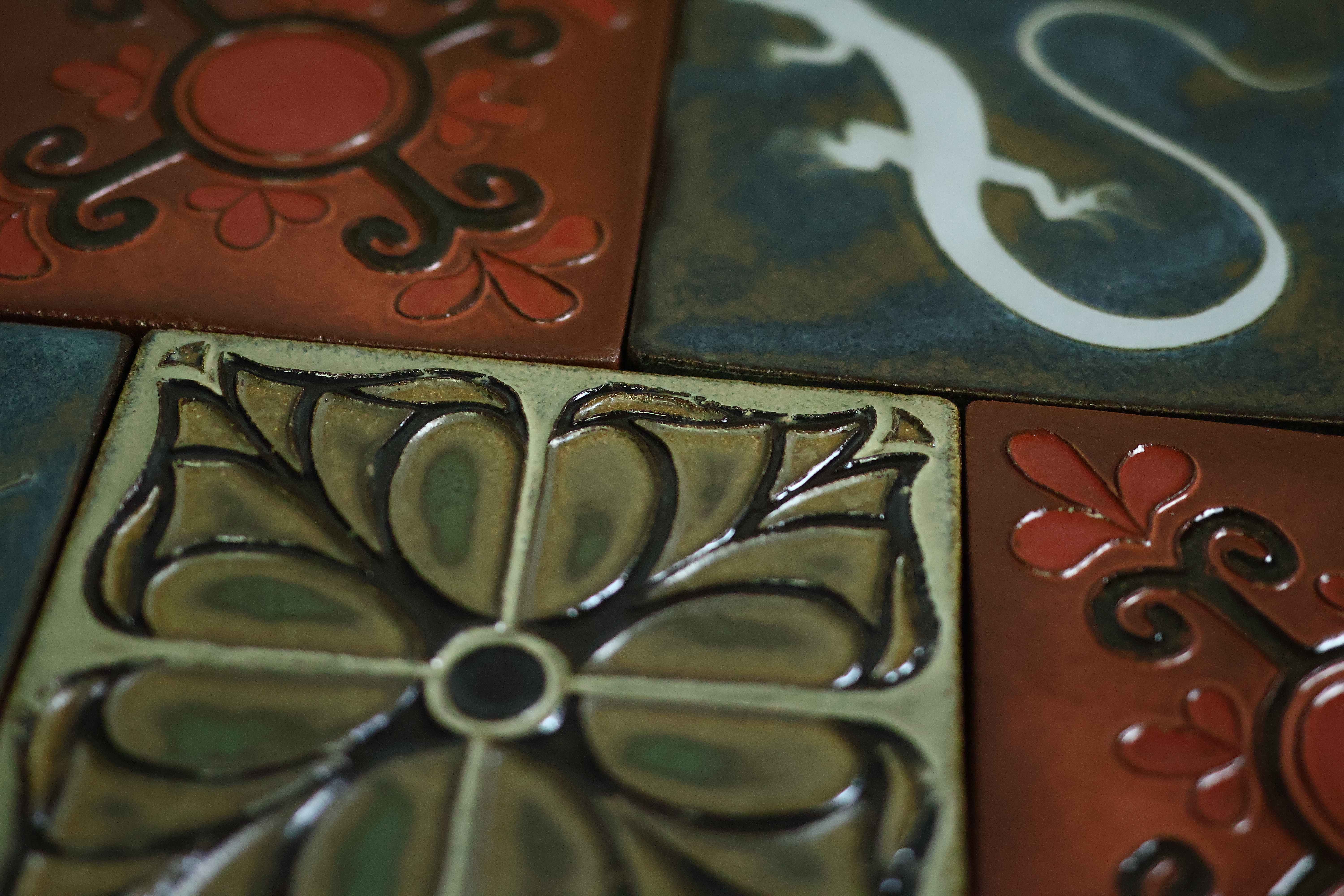 Macro close-up of a green four-petal floral Courtyard tile beside a rust-red medallion tile and a deep-blue lizard tile