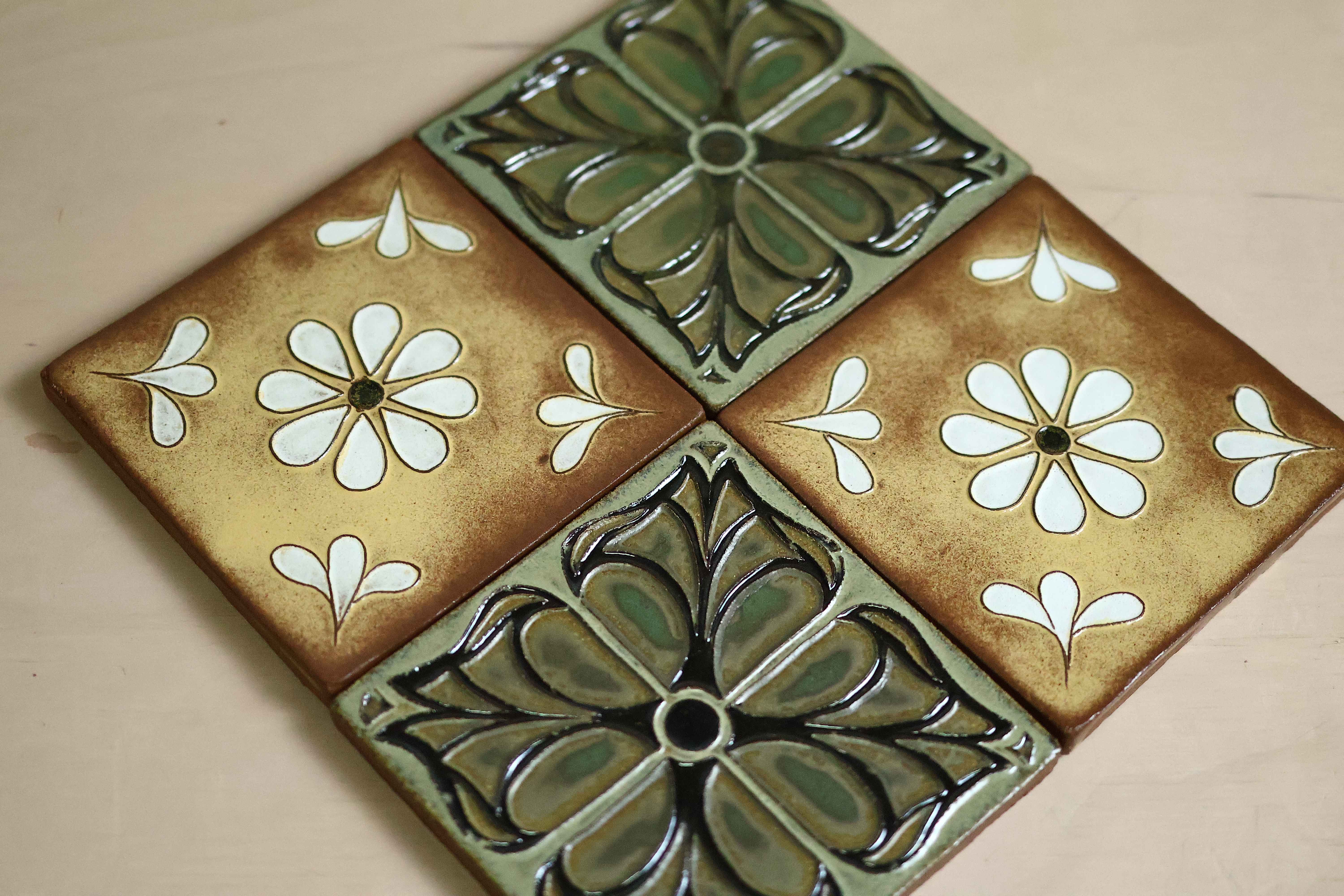 Four Courtyard tiles arranged in a diamond on light wood — two golden daisy tiles and two green floral relief tiles