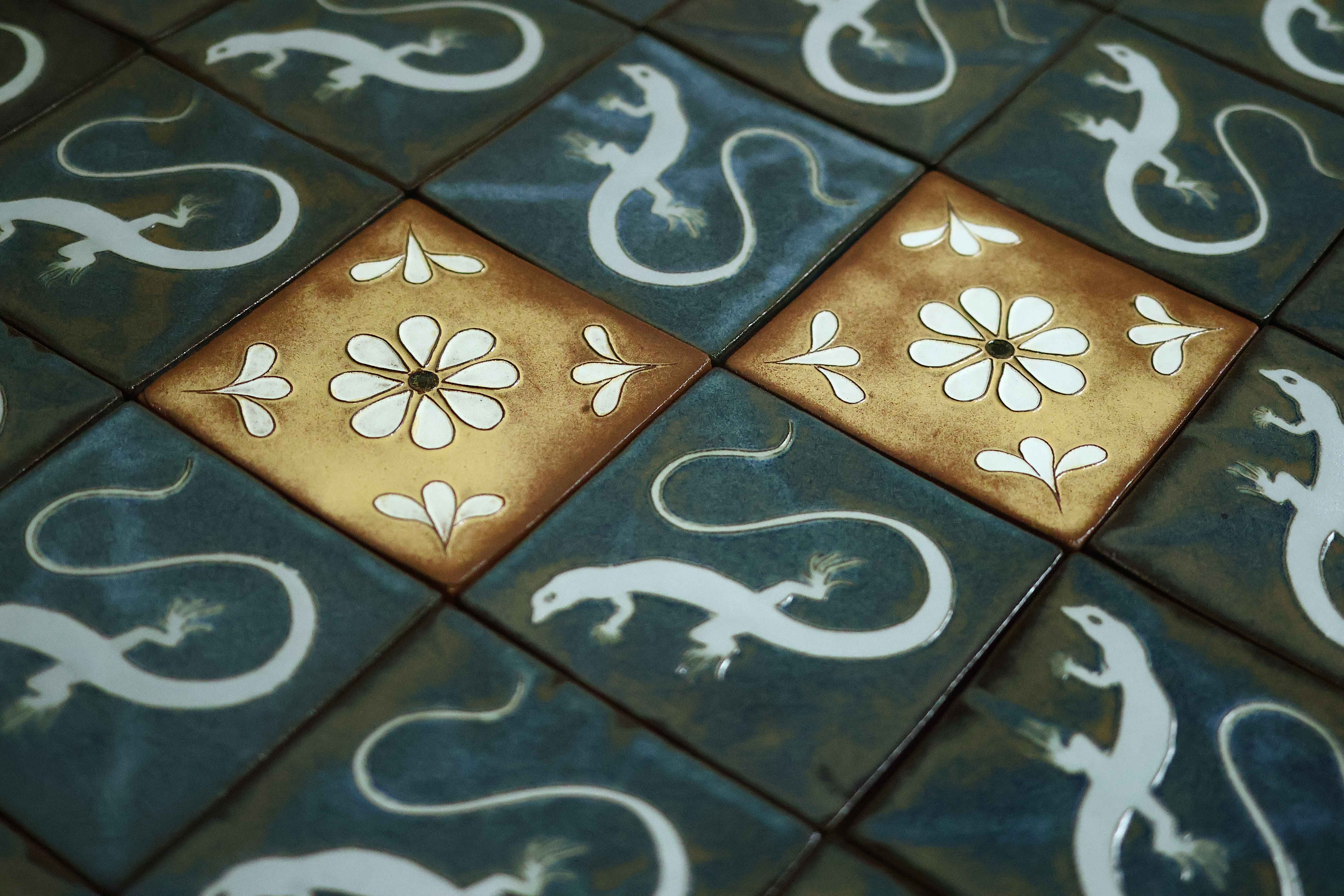 Deep blue Courtyard Series tiles with white lizard silhouettes interspersed with golden tiles bearing white daisies