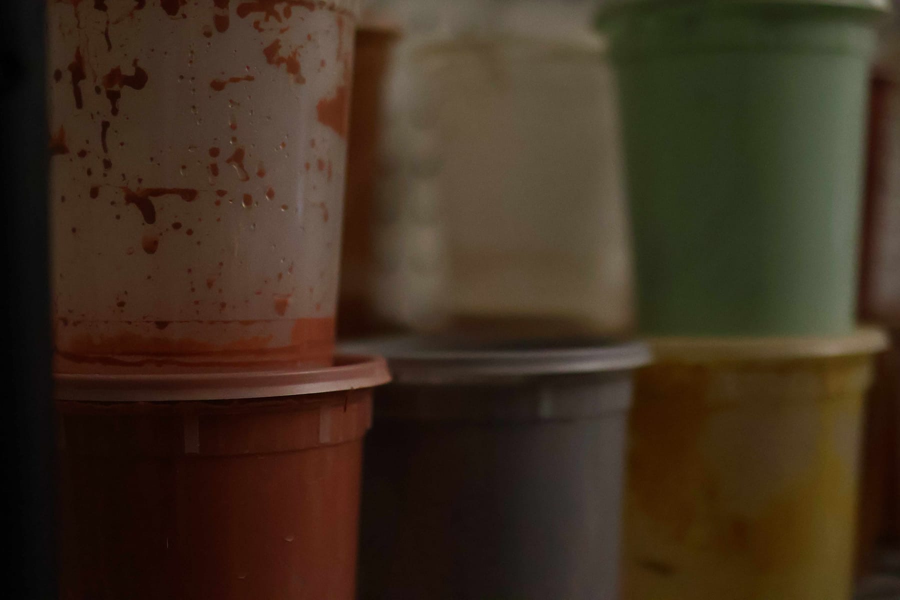 Stacked studio tubs of colored slip, one splattered with terracotta-red